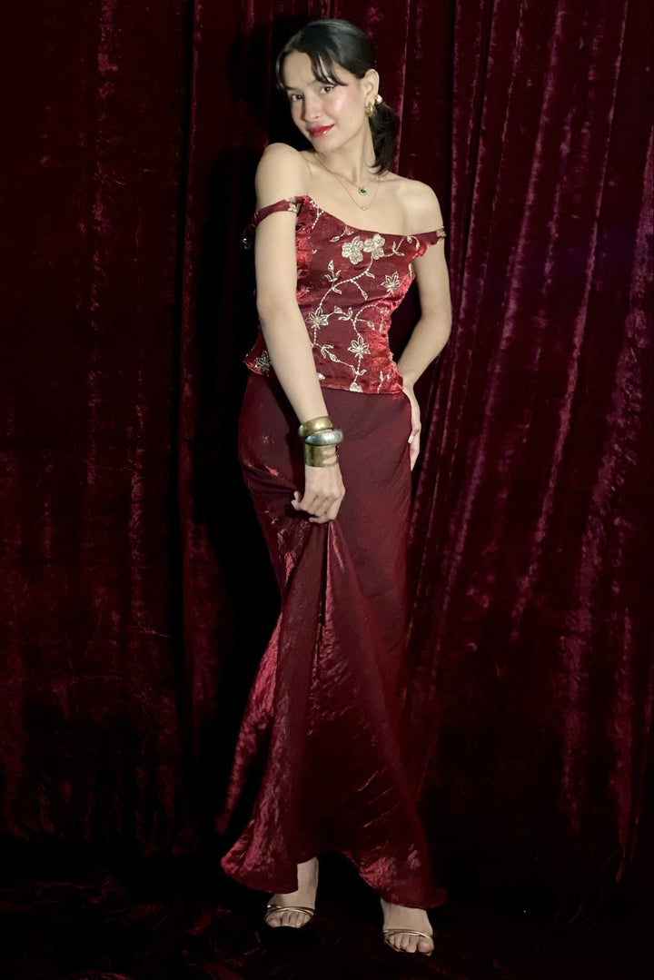 Woman in a red and burgundy evening gown against a dark red curtain
