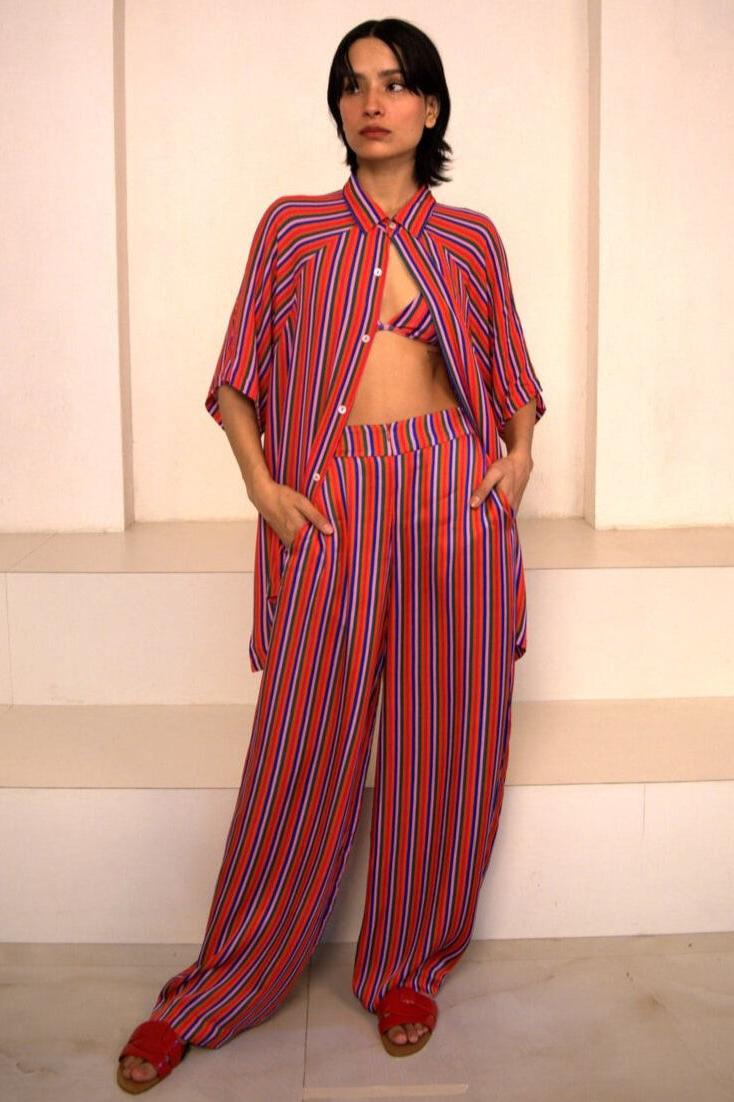 A woman standing and posing in a set of three pieces with candy stripes pattern, including a triangle bikini top, shirt, and trousers.