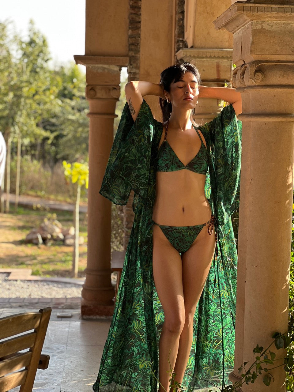 Woman in a green bikini and matching robe standing outdoors with columns in the background