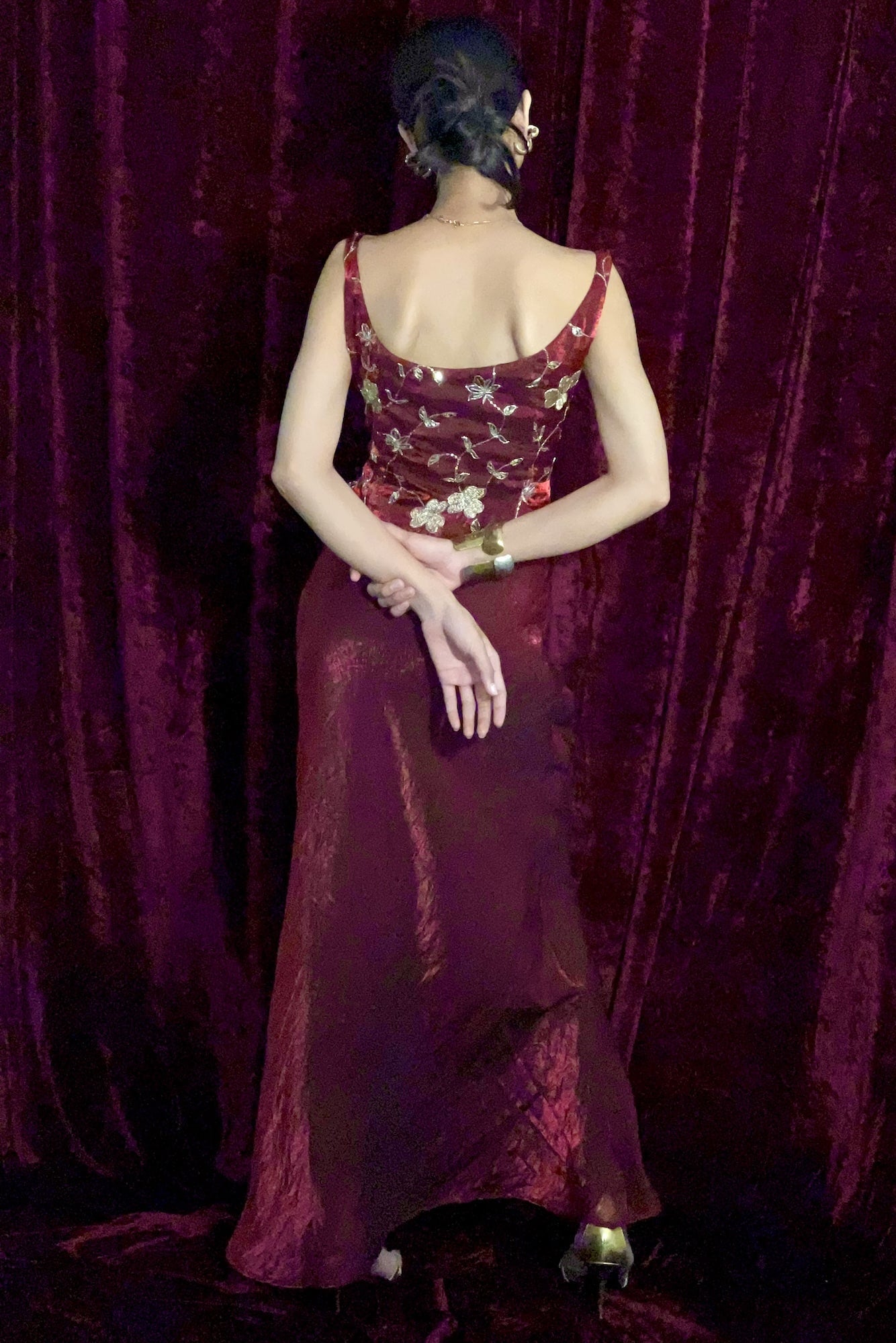 Woman in a burgundy floral dress standing against a purple curtain