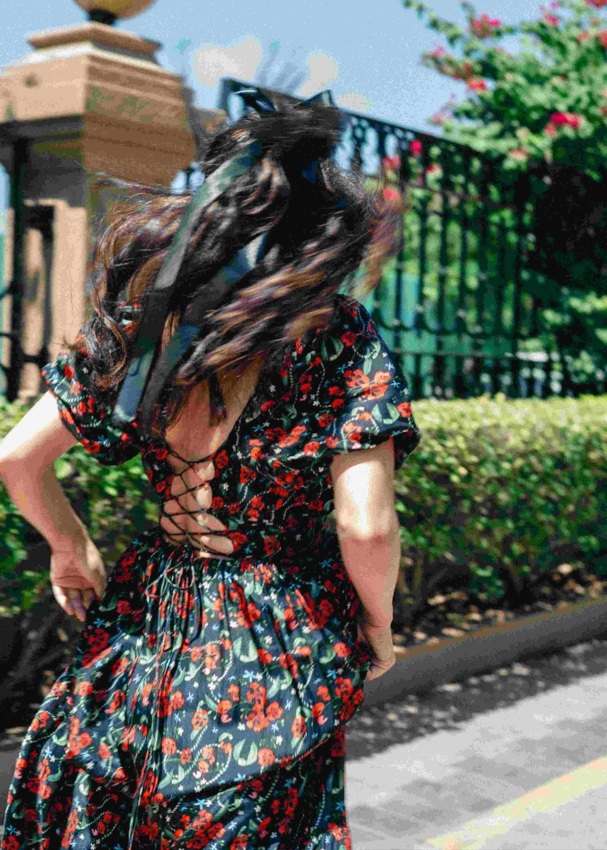 A woman wearing a floral Royal Poinciana back tie-up corset dress with pockets, featuring a deep front neckline and elasticated sleeves, running through a gate with a flowy hemline. swim suit 
swimming suits for women
swimdress for women 
swimdresses for women 
bikini dress 
swim suits for ladies 
swimming dress for ladies 
monokinis 
women's swimdresses 
swimwear
